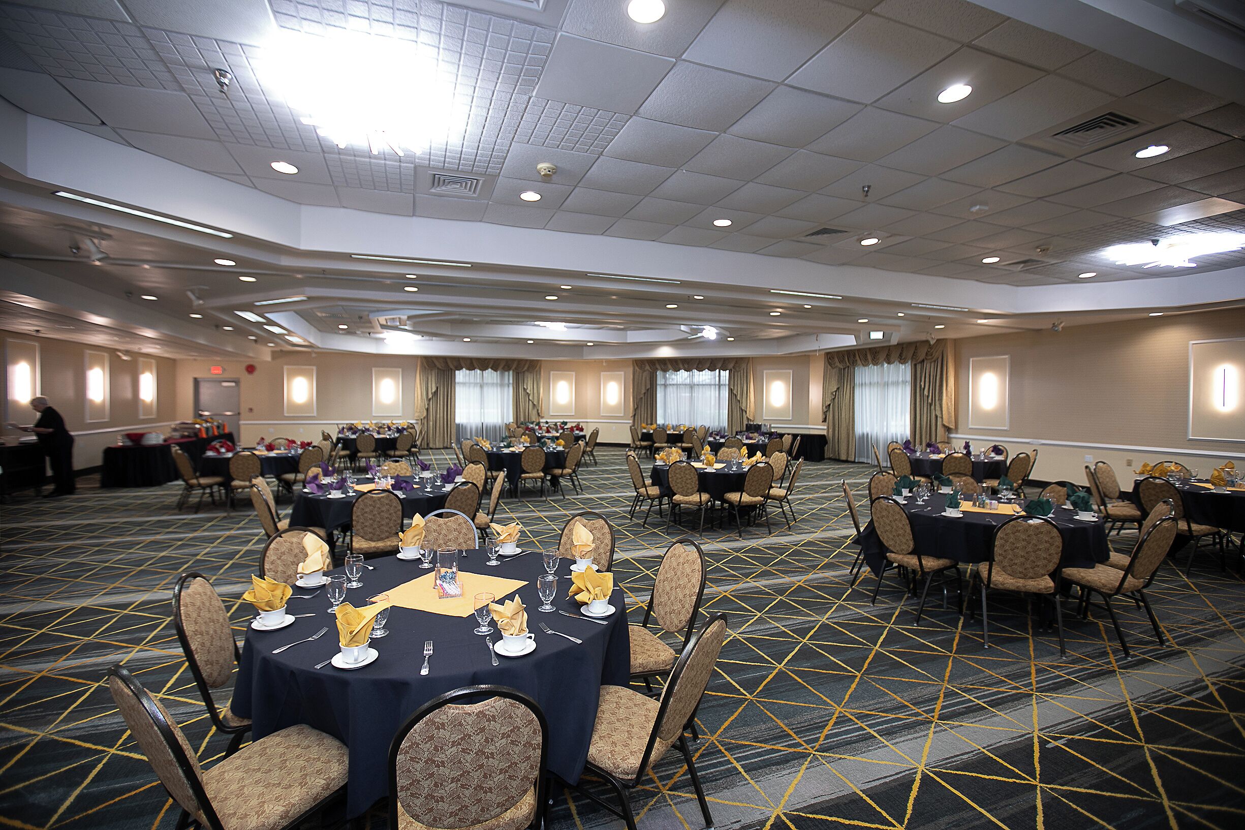 A conference room with multiple tables set for a meeting, equipped with chairs and tables, and a carpeted floor.