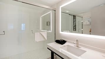 A modern bathroom with a glass shower enclosure, a white sink with a black towel, and a large mirror.