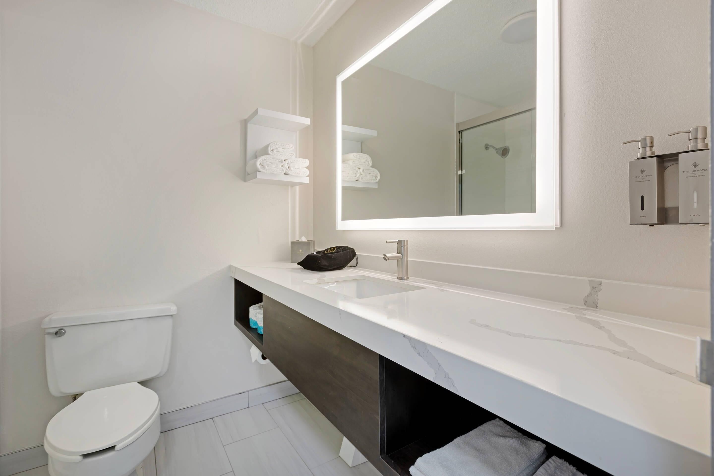 A modern bathroom with a white toilet, a large mirror, a white sink, and a dark vanity.