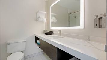 A modern bathroom with a white toilet, a large mirror, a white sink, and a dark vanity.