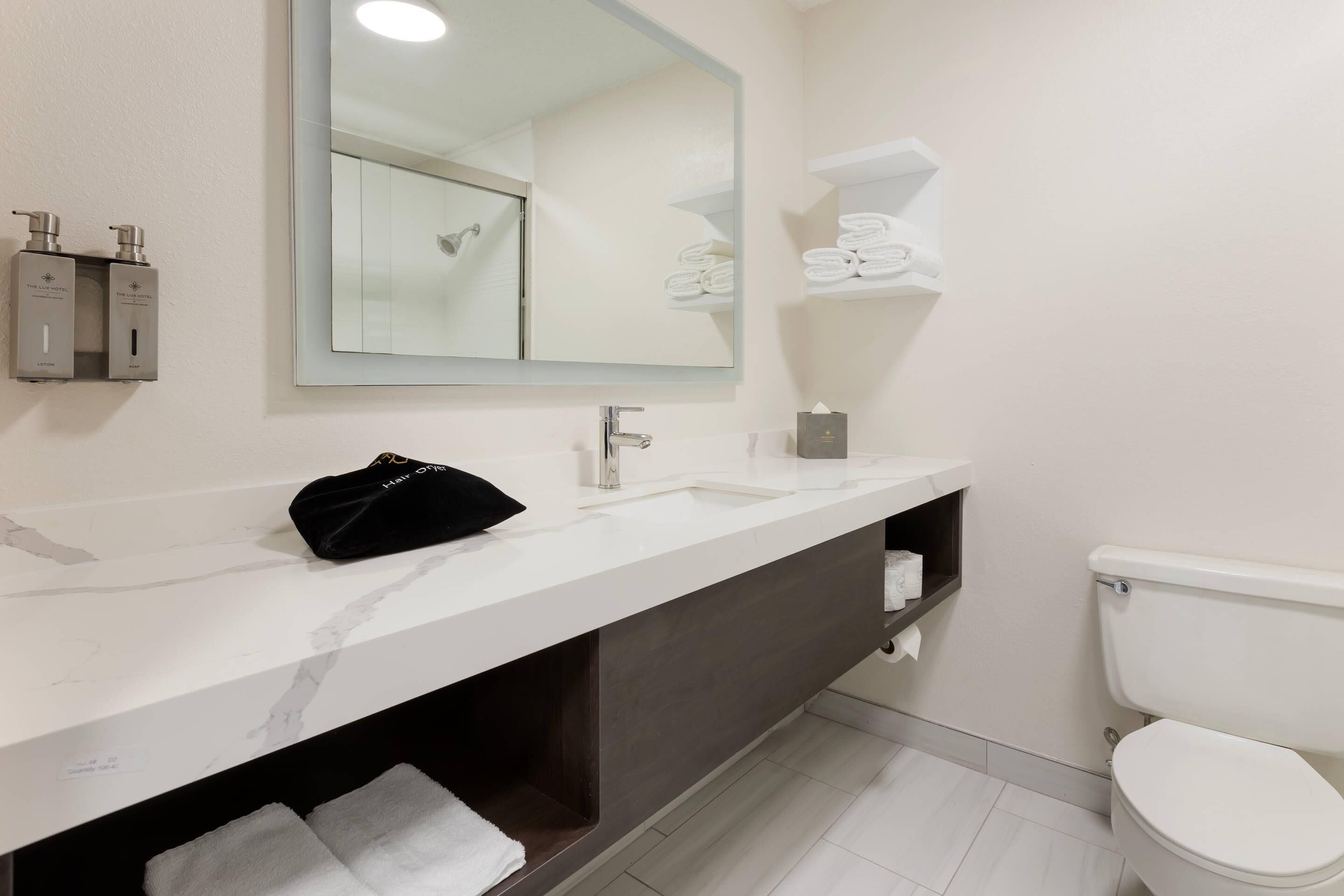 A modern bathroom with a marble sink, a large mirror, a toilet, and neatly arranged towels.