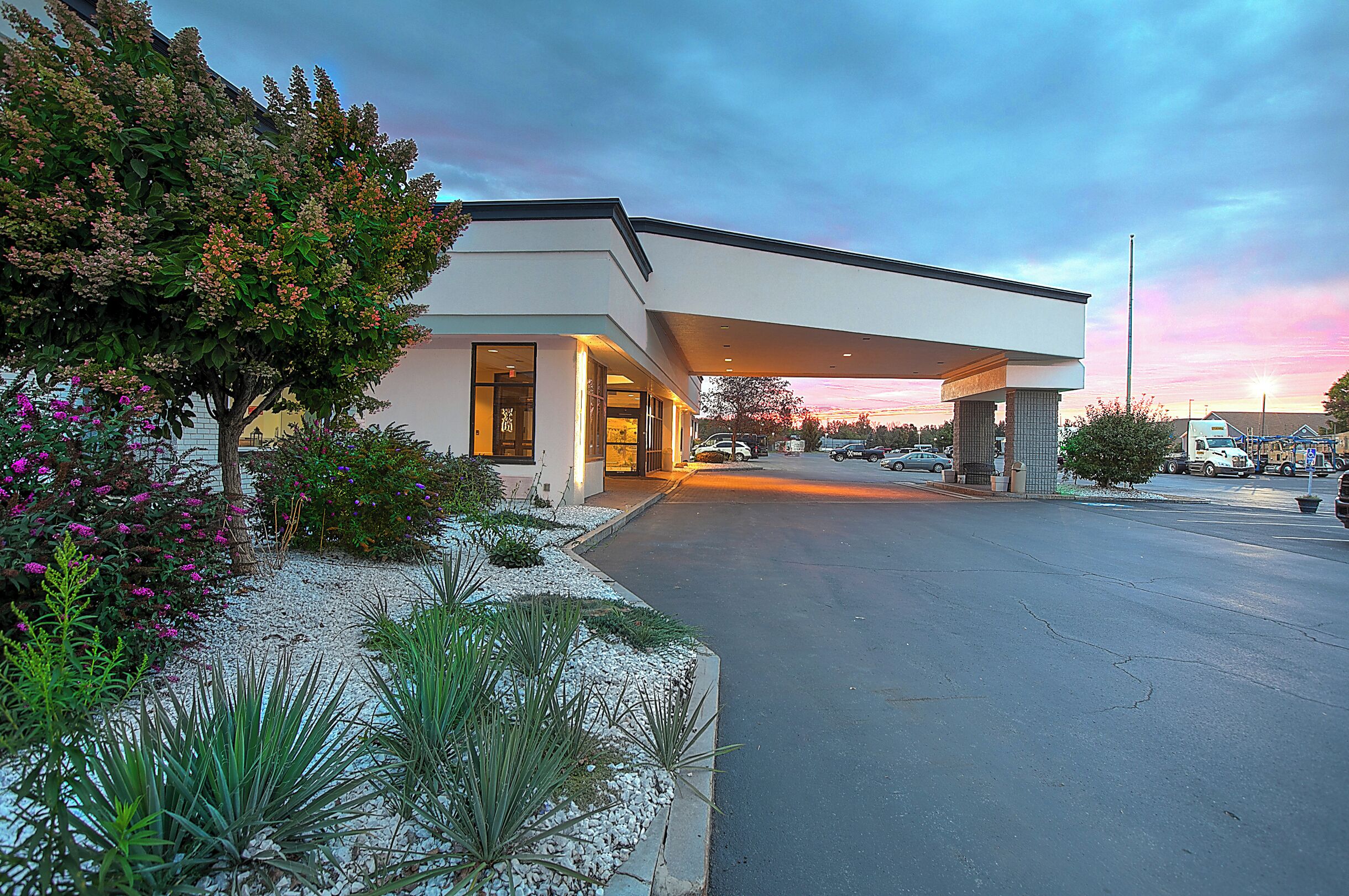 A modern building with a covered entrance, a parking lot, and a sunset sky.