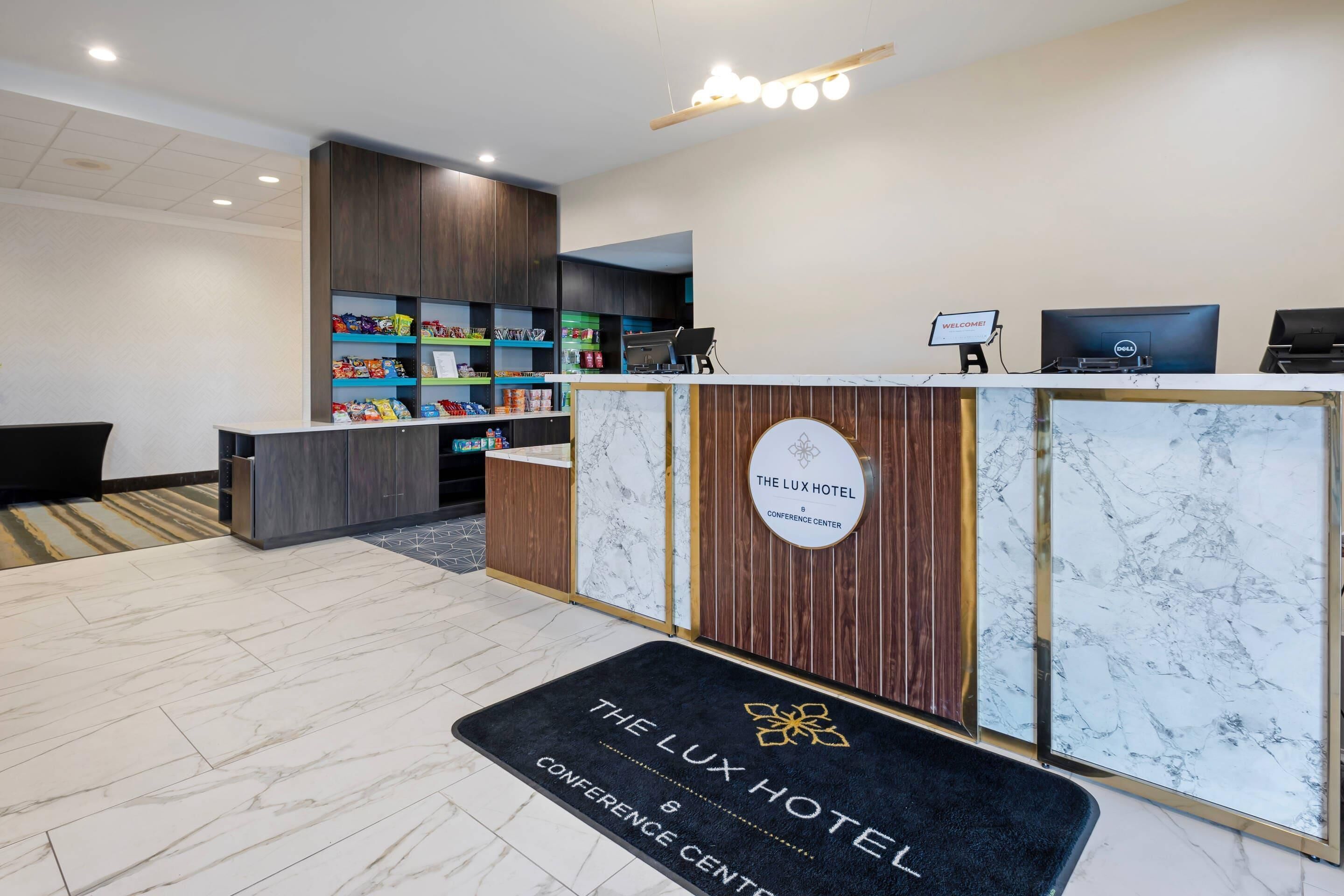 A reception area with a marble floor, a reception desk with a sign reading "The Lux Hotel Conference Center," and a welcome sign above the desk.
