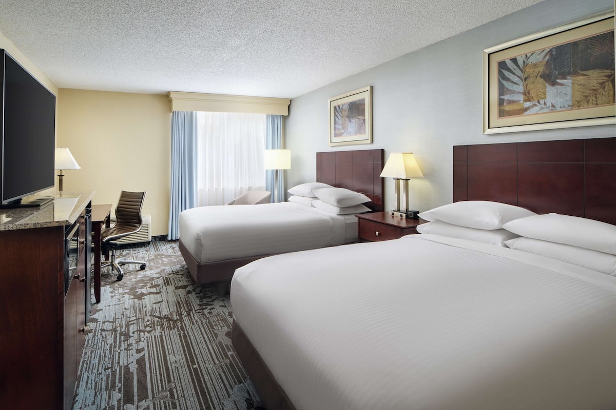A hotel room with two beds, a desk with a chair, a television, and a window with curtains.