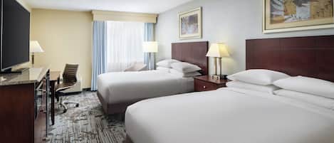 A hotel room with two beds, a desk with a chair, a television, and a window with curtains.