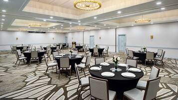 A conference room with multiple tables and chairs, chandeliers, and a carpeted floor.