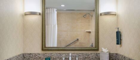 A bathroom with a granite countertop, a sink, a mirror, and a shower with a towel rack.