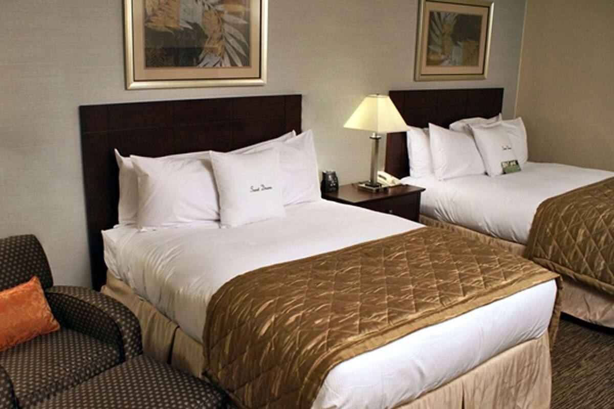 A hotel room with two beds, a chair, and two lamps.