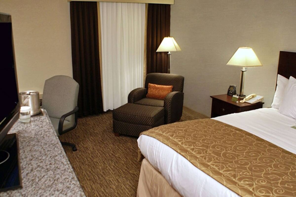 A hotel room with a bed, two chairs, a desk, a lamp, and a telephone.