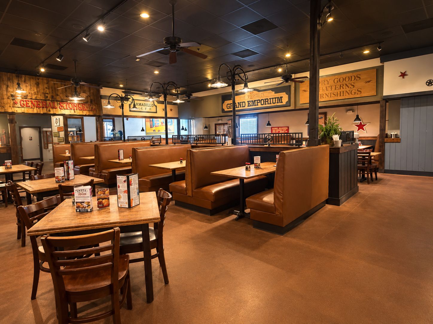 A restaurant interior with booths and tables, wooden flooring, and ceiling fans.