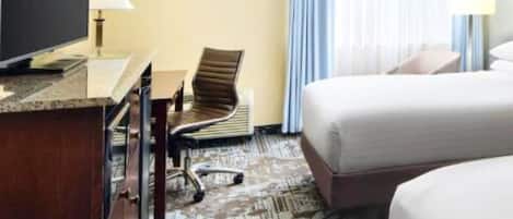 A hotel room with a bed, a desk with a chair, a television, and a window with curtains.