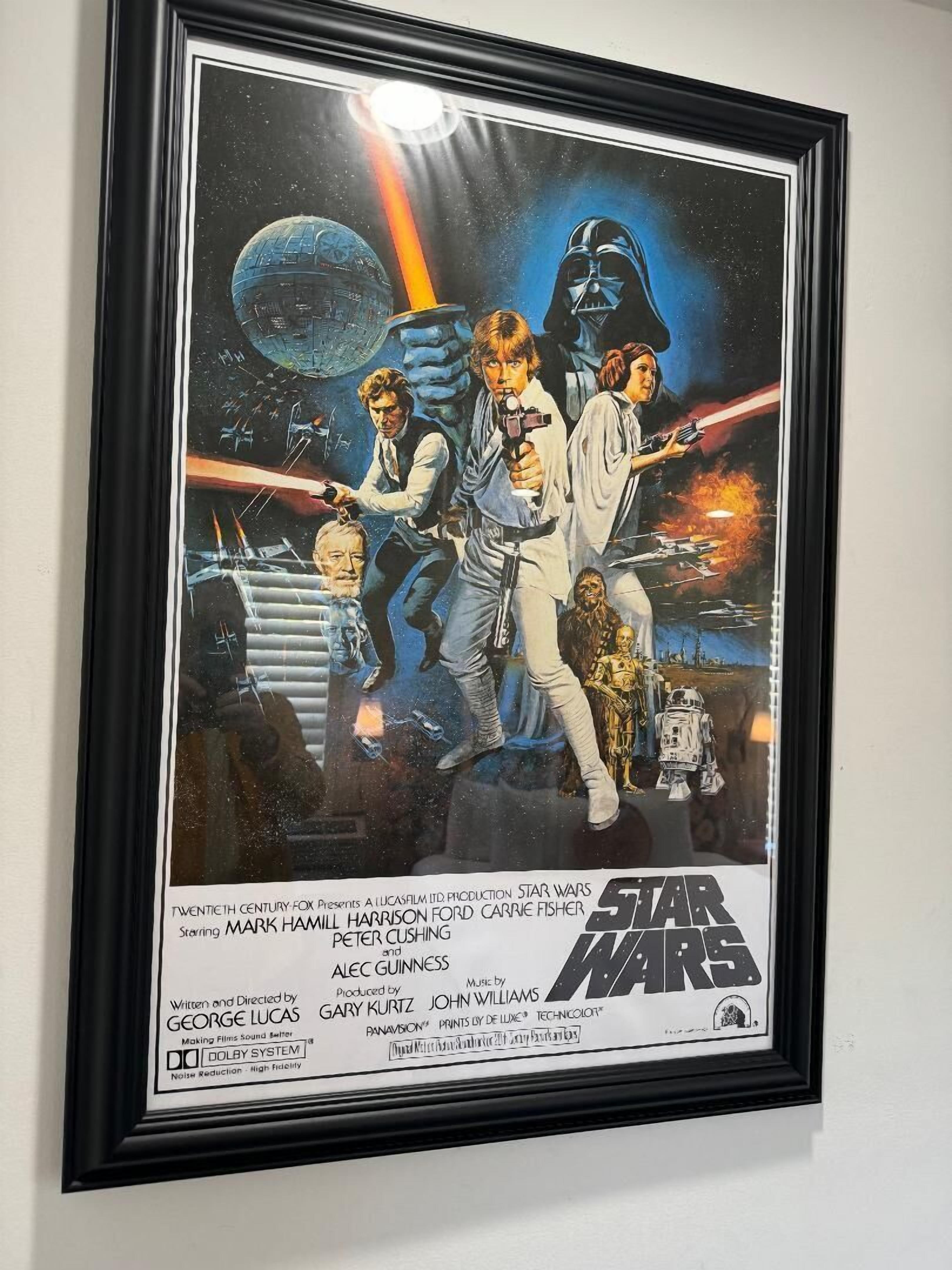 A framed movie poster of Star Wars with characters and spaceships.
