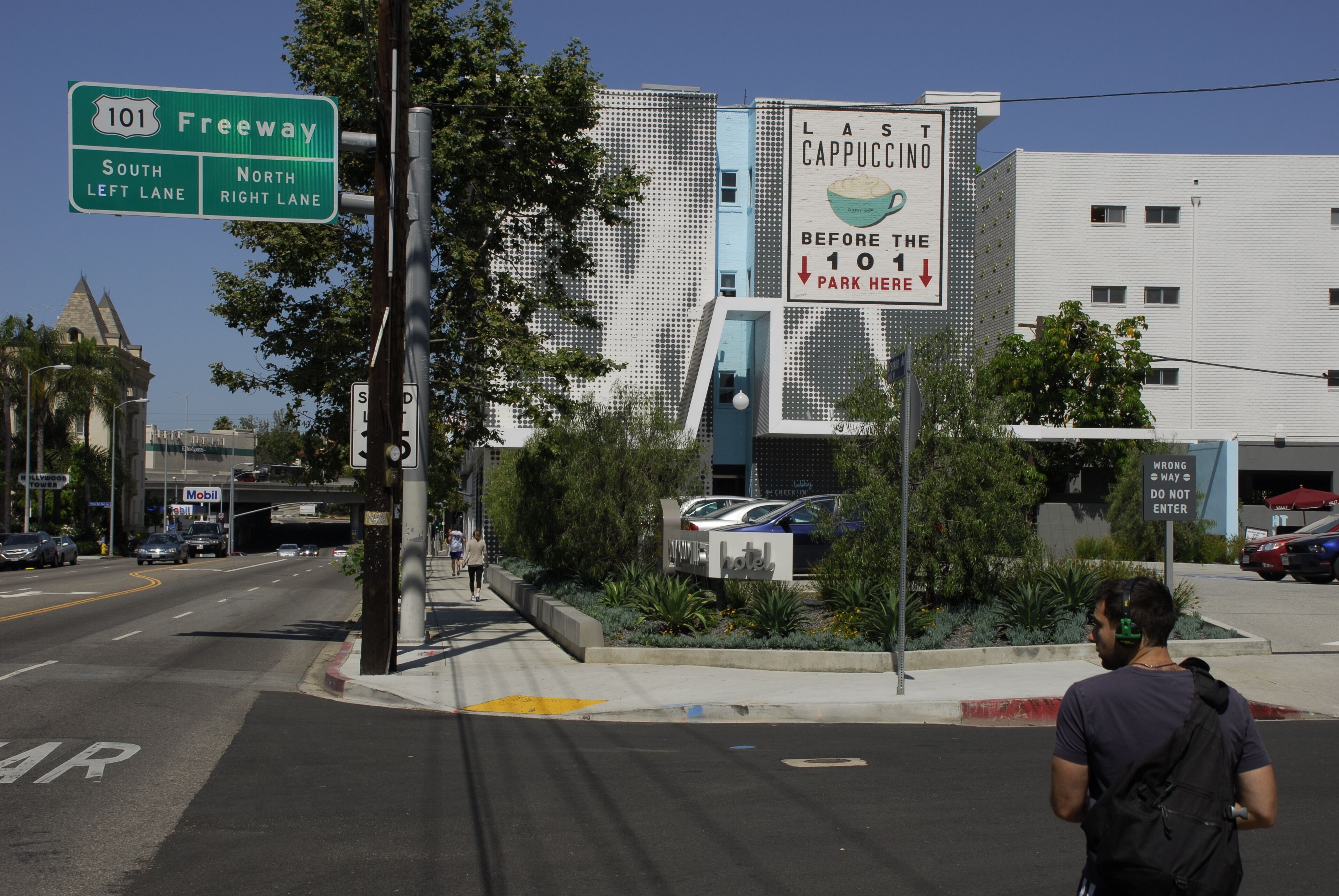 A street view with a sign for the 101 Freeway, a building with a sign for Last Cappuccino, and a hotel sign.