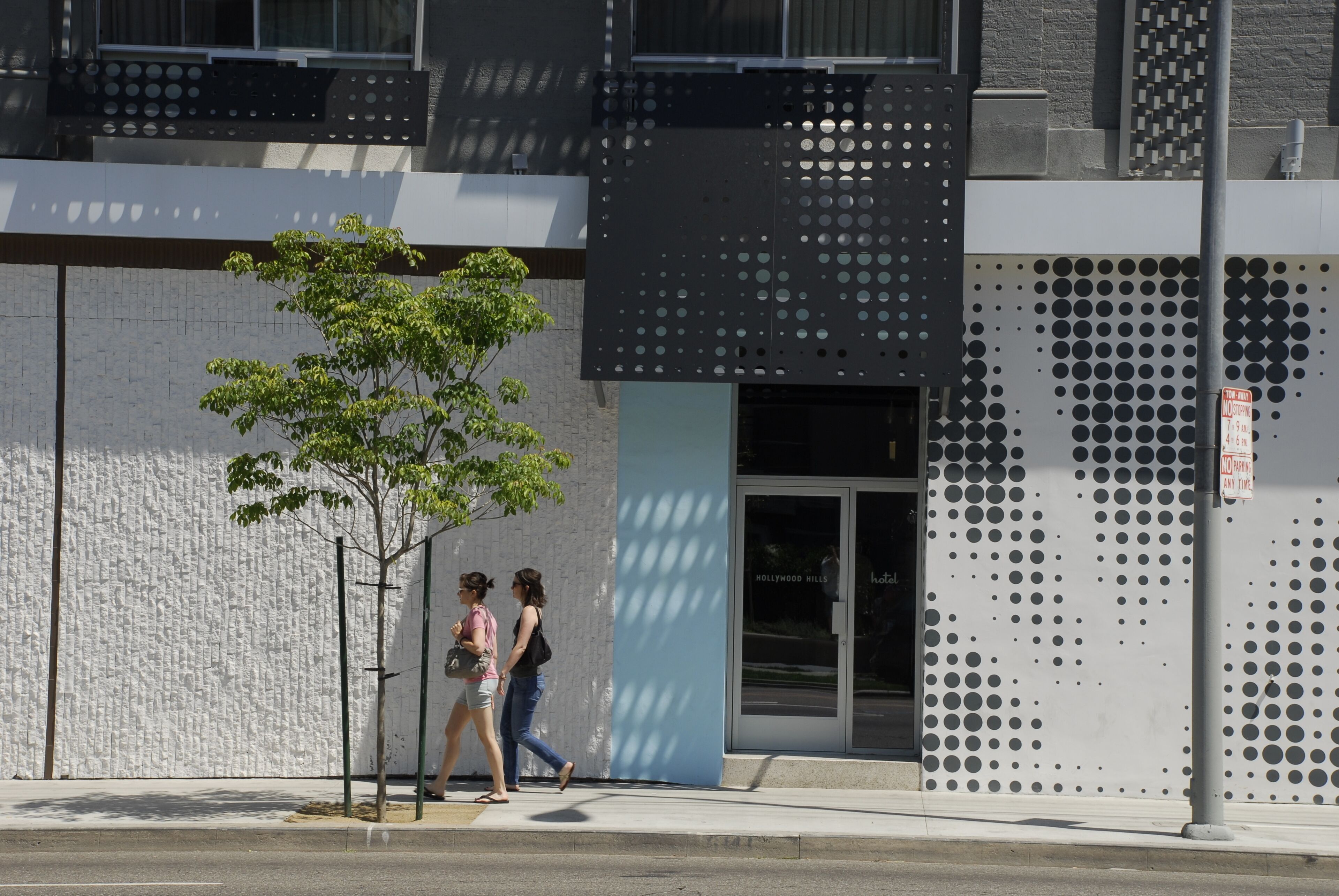 A modern building with a textured facade, a tree in front, and a patterned wall.