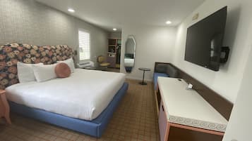 Una habitación de hotel con cama, mesita de noche, espejo, televisor y una pequeña mesa redonda.