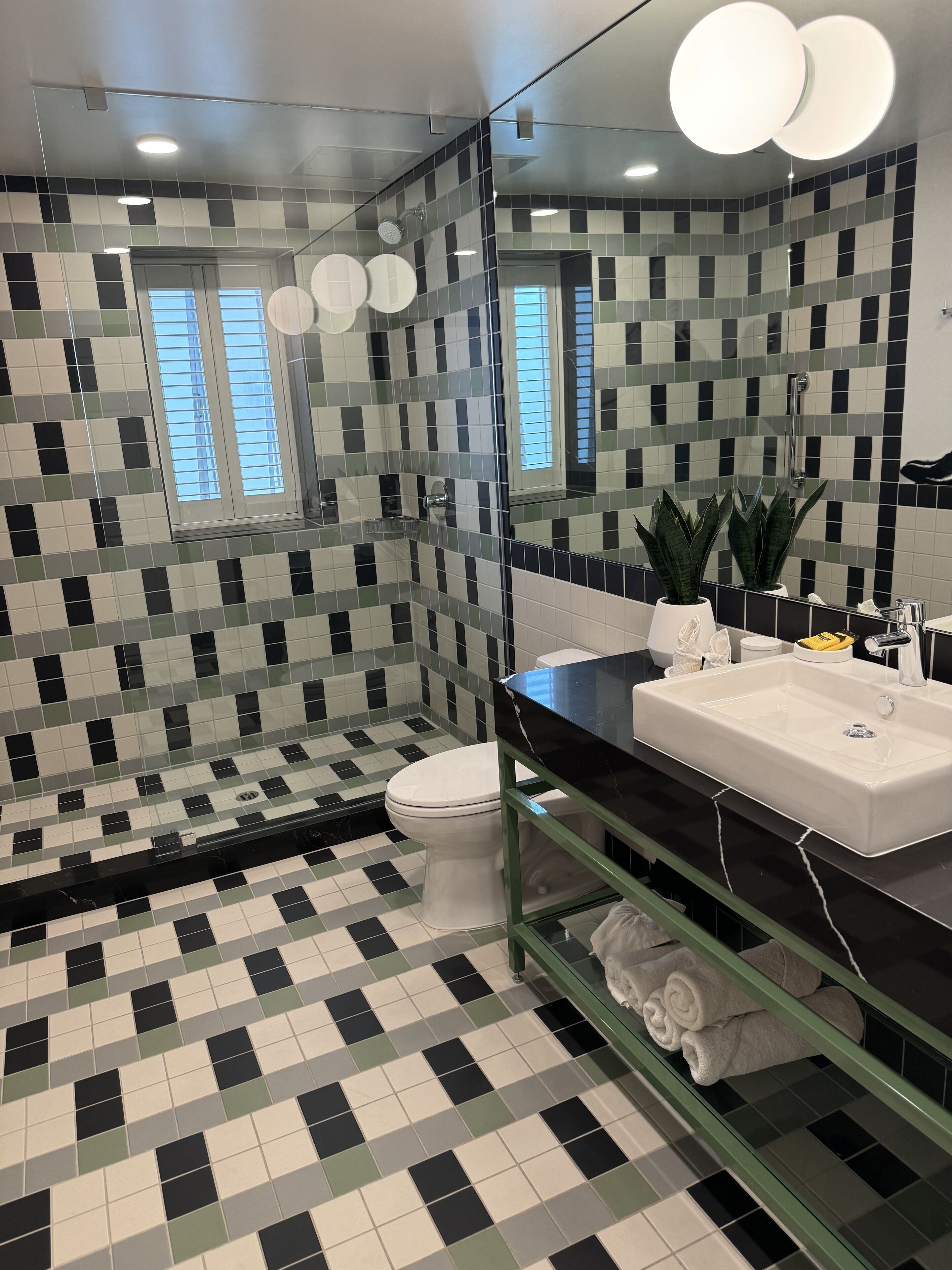 A bathroom with a checkered floor, a white toilet, a sink with a mirror, and a shower area.