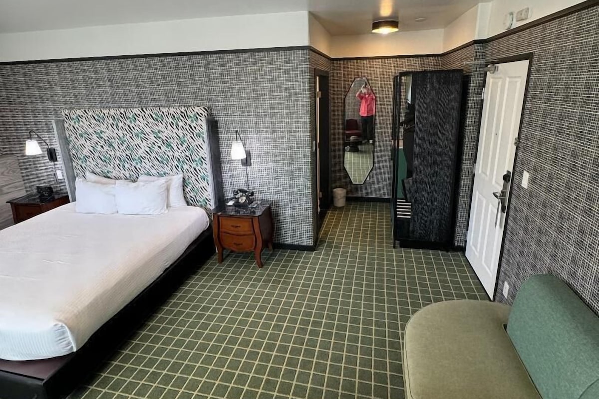 Een hotelkamer met een groot bed, een kleine tafel met een plant, een bank en een spiegel.