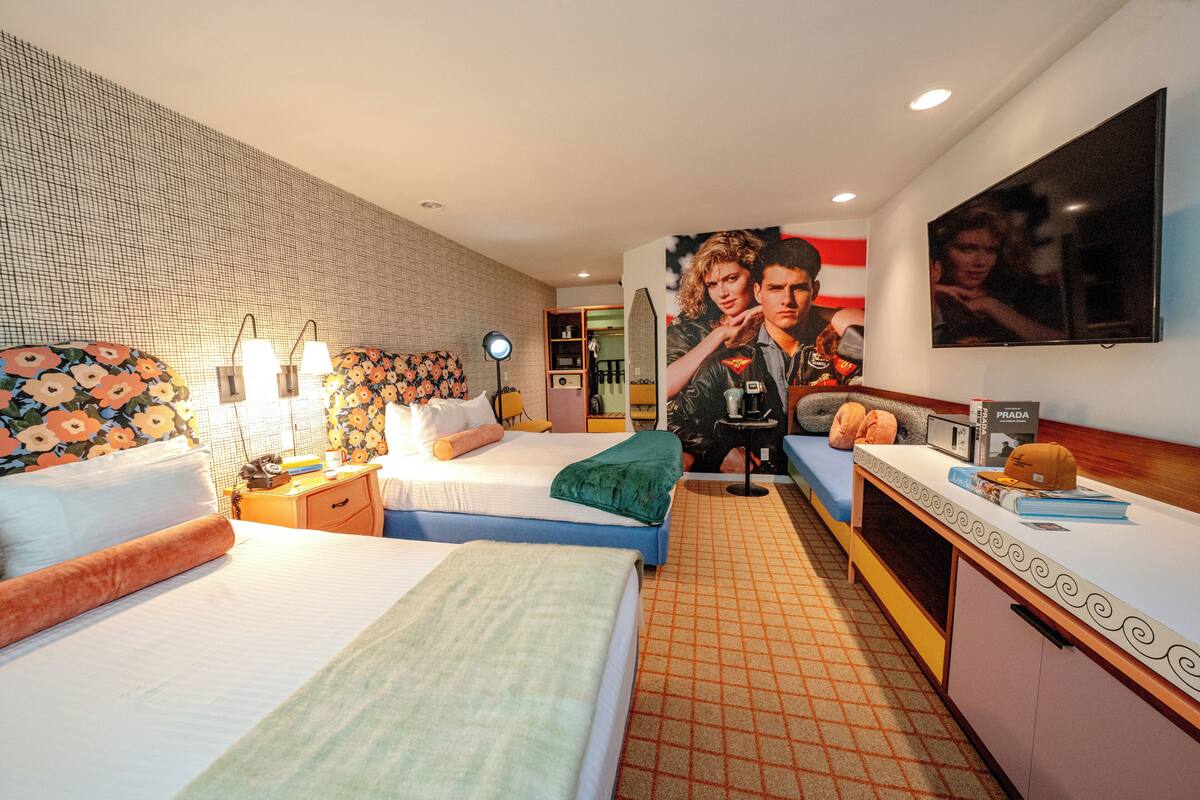 Een hotelkamer met twee bedden, een bureau, een televisie en een groot poster aan de muur.