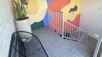 A small outdoor area with a colorful mural on the wall, a potted plant, and a black chair.