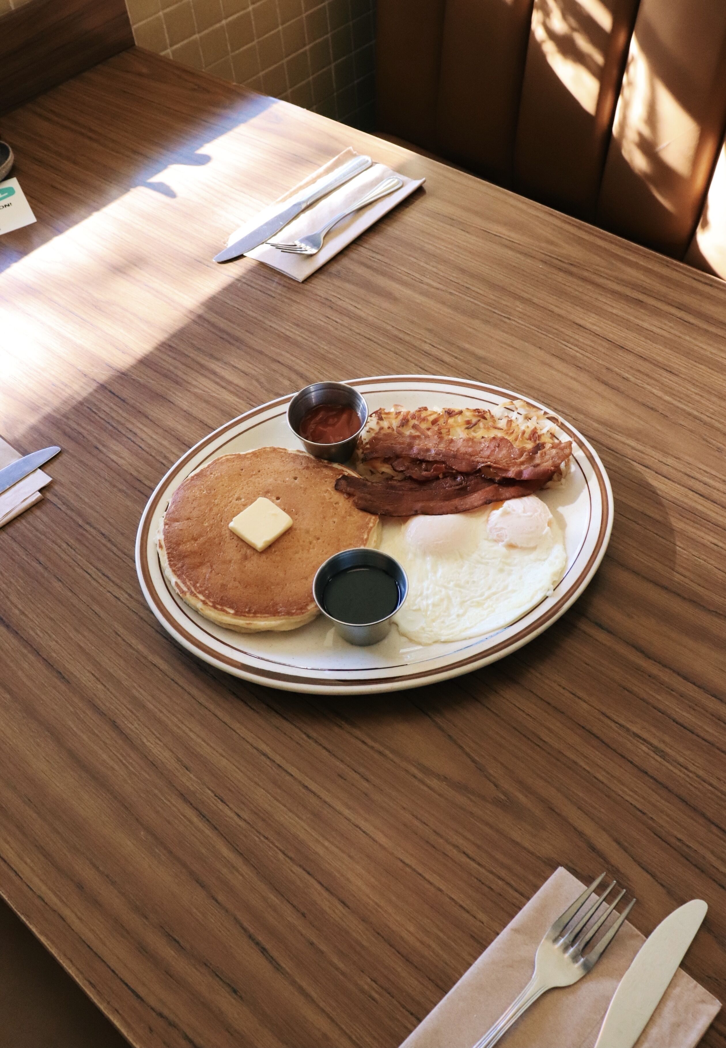 A breakfast plate with pancakes, eggs, and bacon on a wooden table.