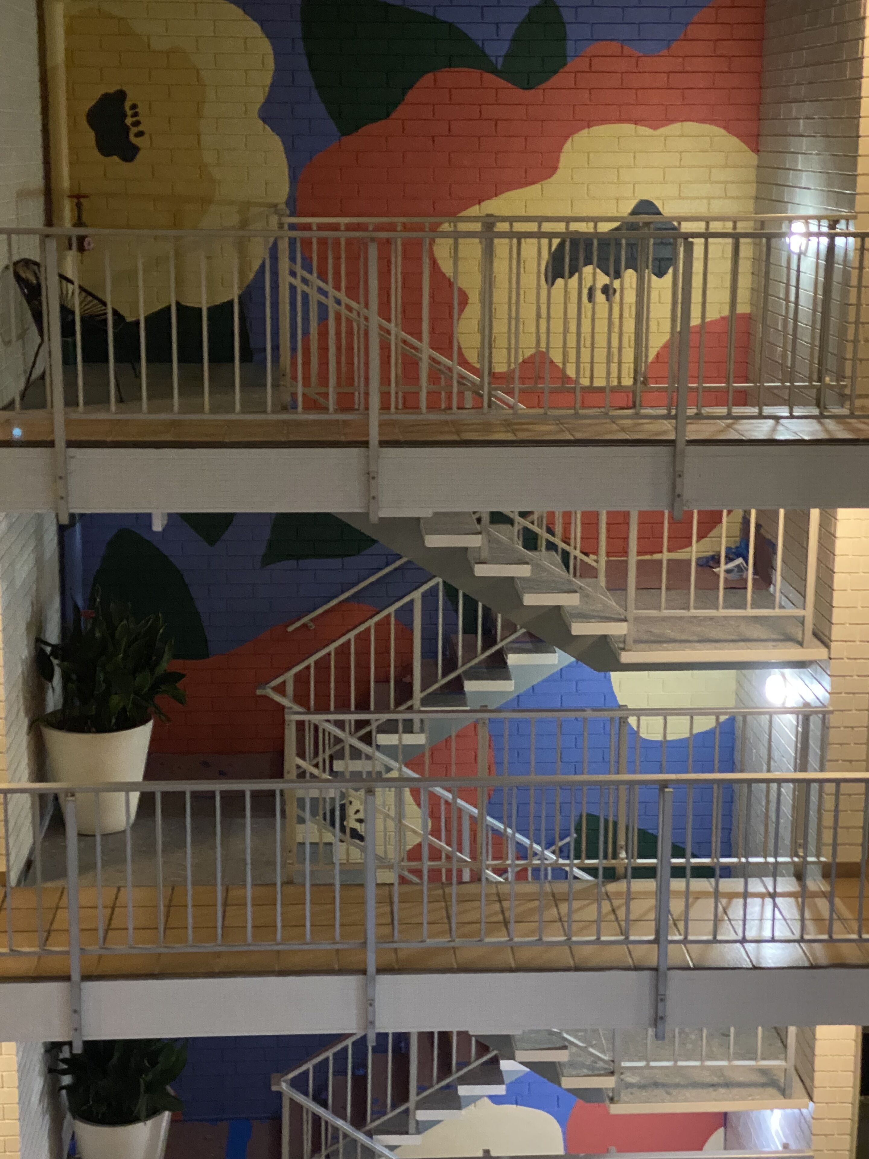 Un intérieur à plusieurs niveaux, avec un escalier, des rampes en métal et une fresque colorée sur les murs.