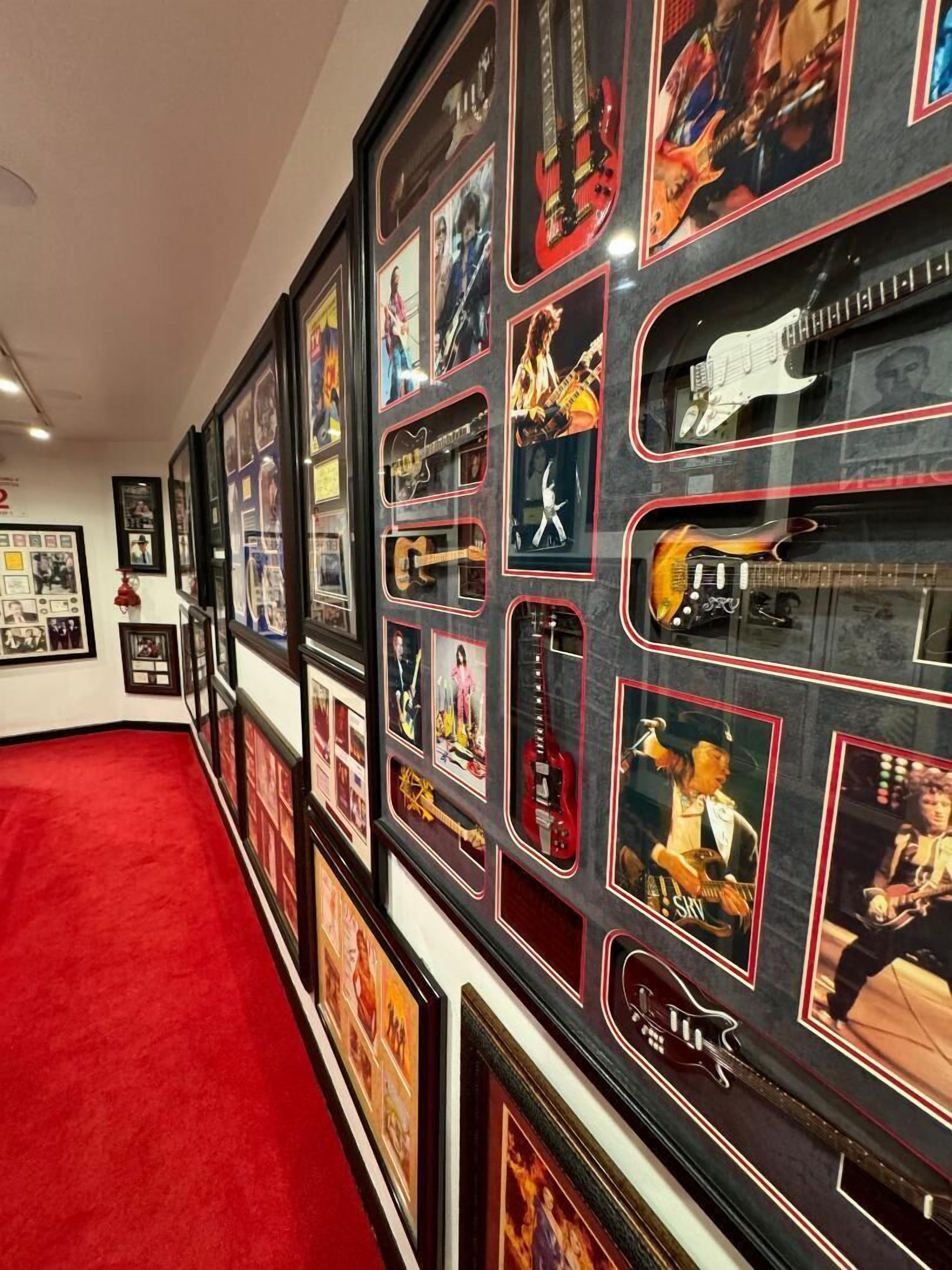 Una pared con cuadros enmarcados y guitarras, una alfombra roja y un techo blanco.