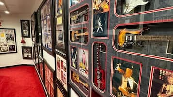 Una pared con cuadros enmarcados y guitarras, una alfombra roja y un techo blanco.