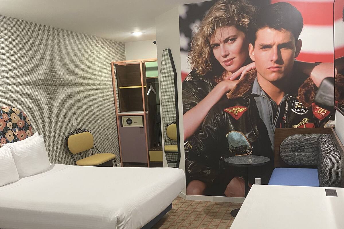 Een hotelkamer met een groot bed, een klein bureau, een stoel, een garderobe en een poster aan de muur.