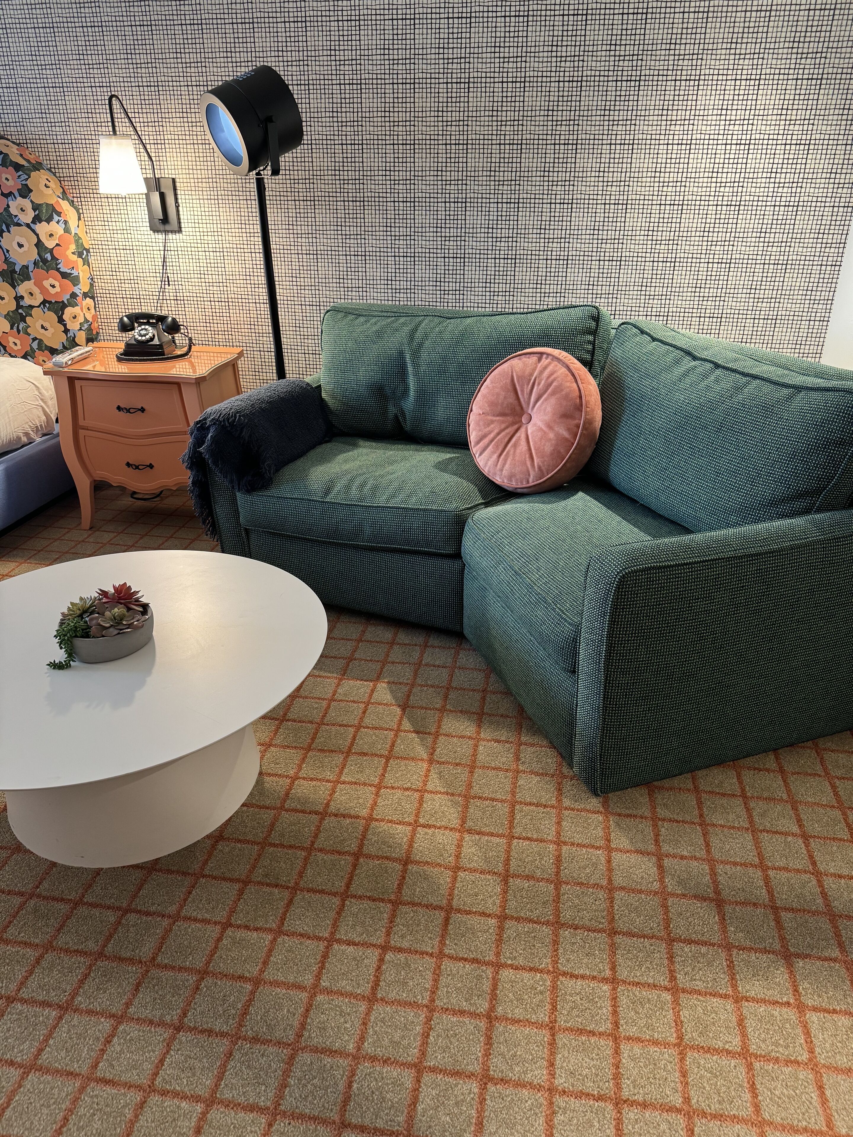 A room with a green sofa, a white coffee table, a patterned rug, a small plant, a vintage telephone, and a lamp.