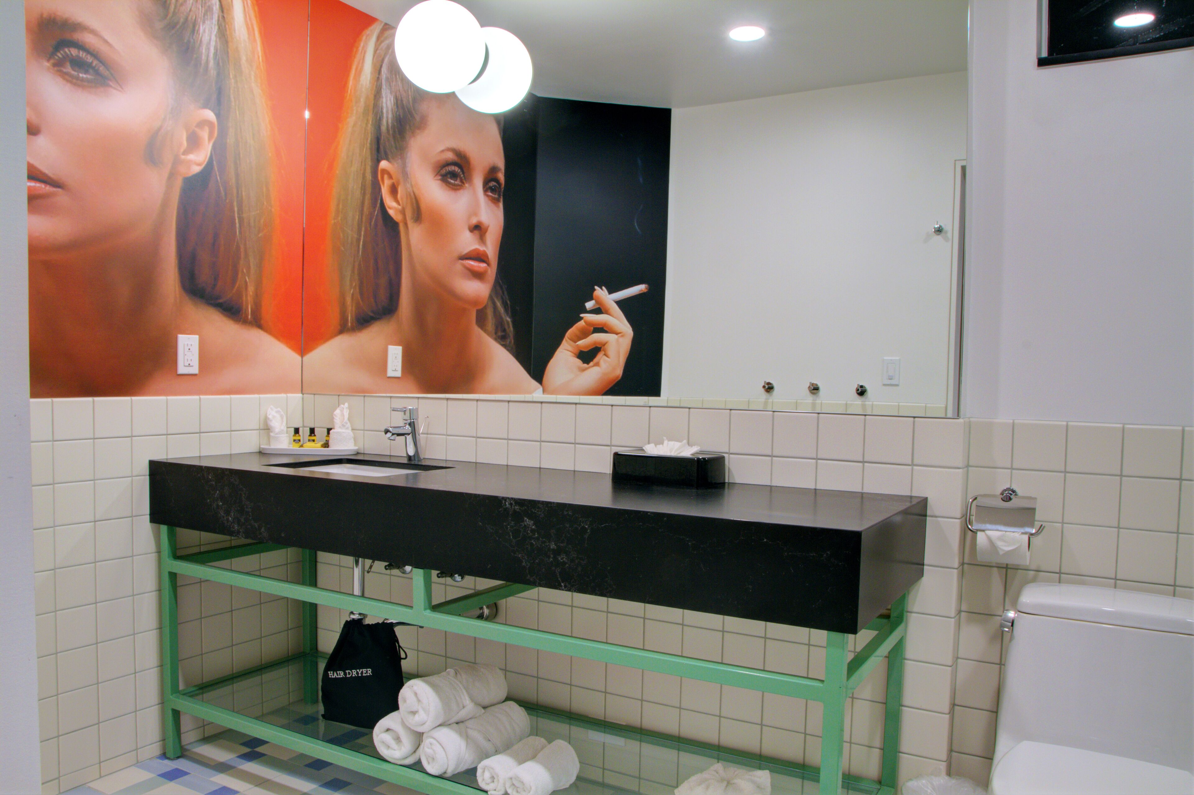 Um banheiro com pia preta, prateleiras verdes, um espelho e um vaso sanitário.