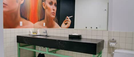 Um banheiro com pia preta, prateleiras verdes, um espelho e um vaso sanitário.