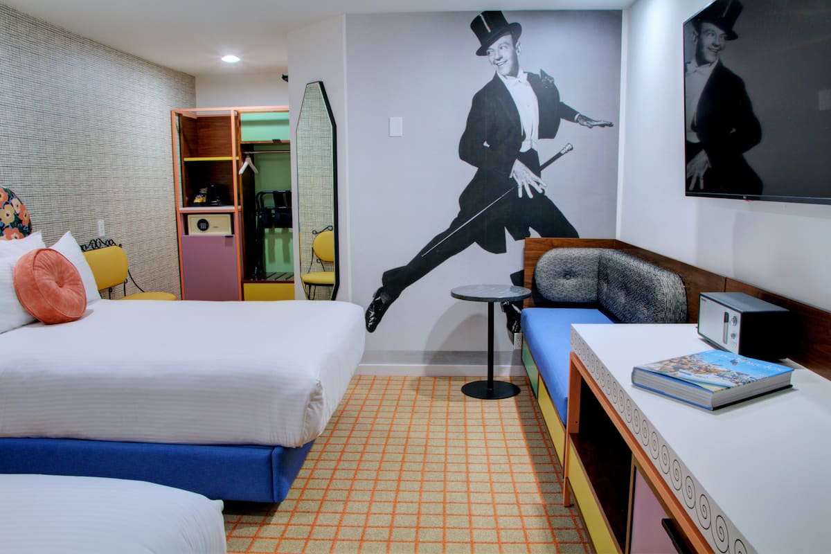 Een hotelkamer met een bed, een bank, een klein tafeltje en een wand met een groot poster.