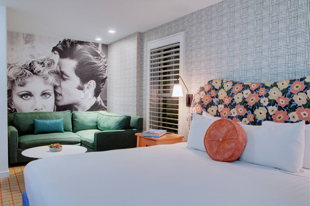 Een slaapkamer met een groene bank, een wit bed met bloemenkussens, een kleine tafel en een groot behang met bloemenmotieven.