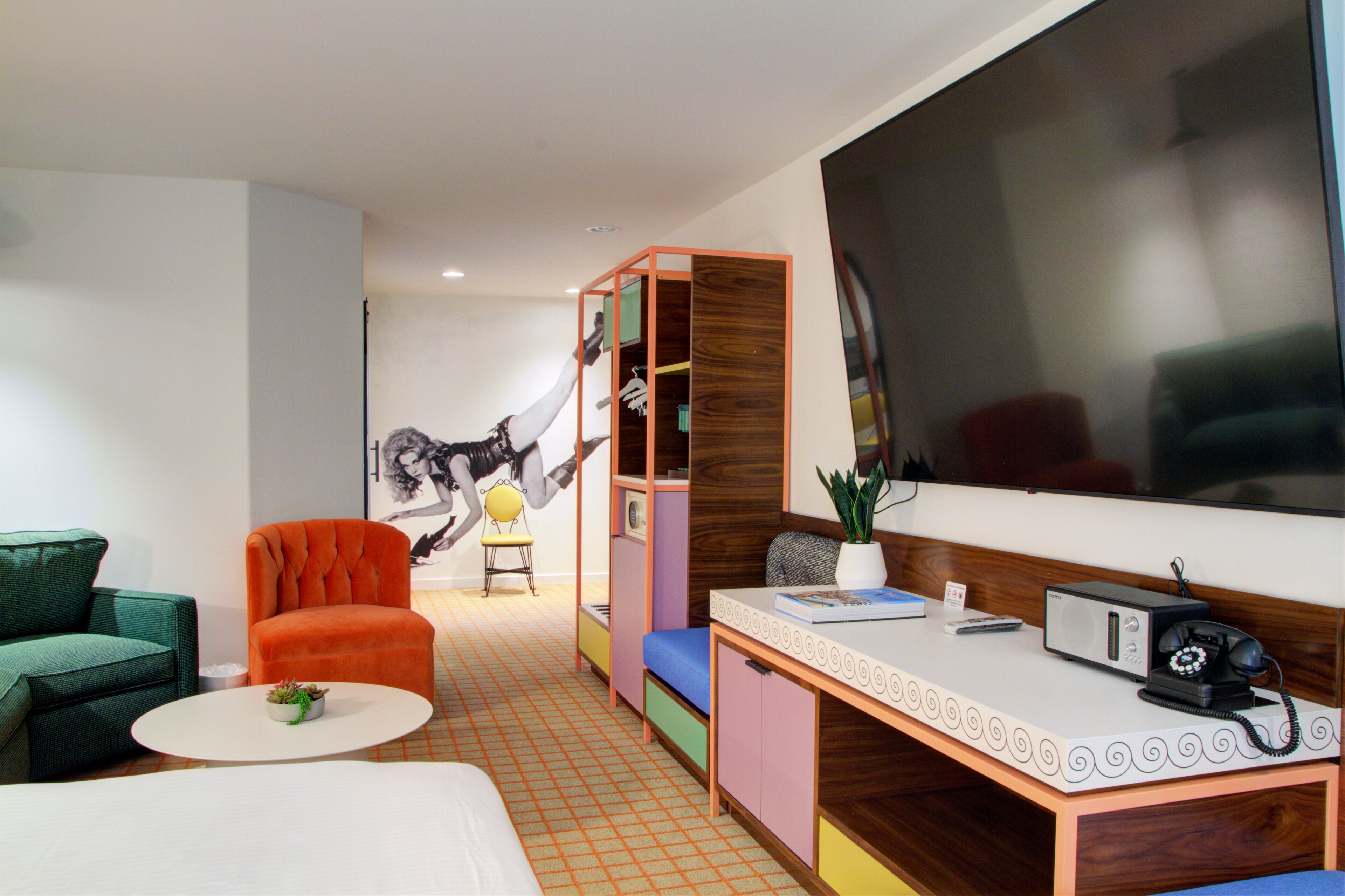 Una habitación de hotel moderna con una cama grande, un escritorio con teléfono, una silla, un sofá y un mueble de colores.