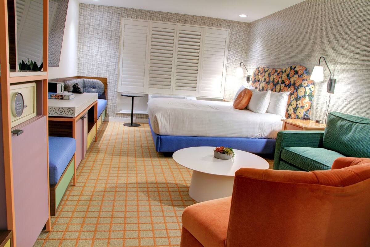 Een compacte hotelkamer met een bed, een bureau, een stoel, een klein tafeltje en een bank.