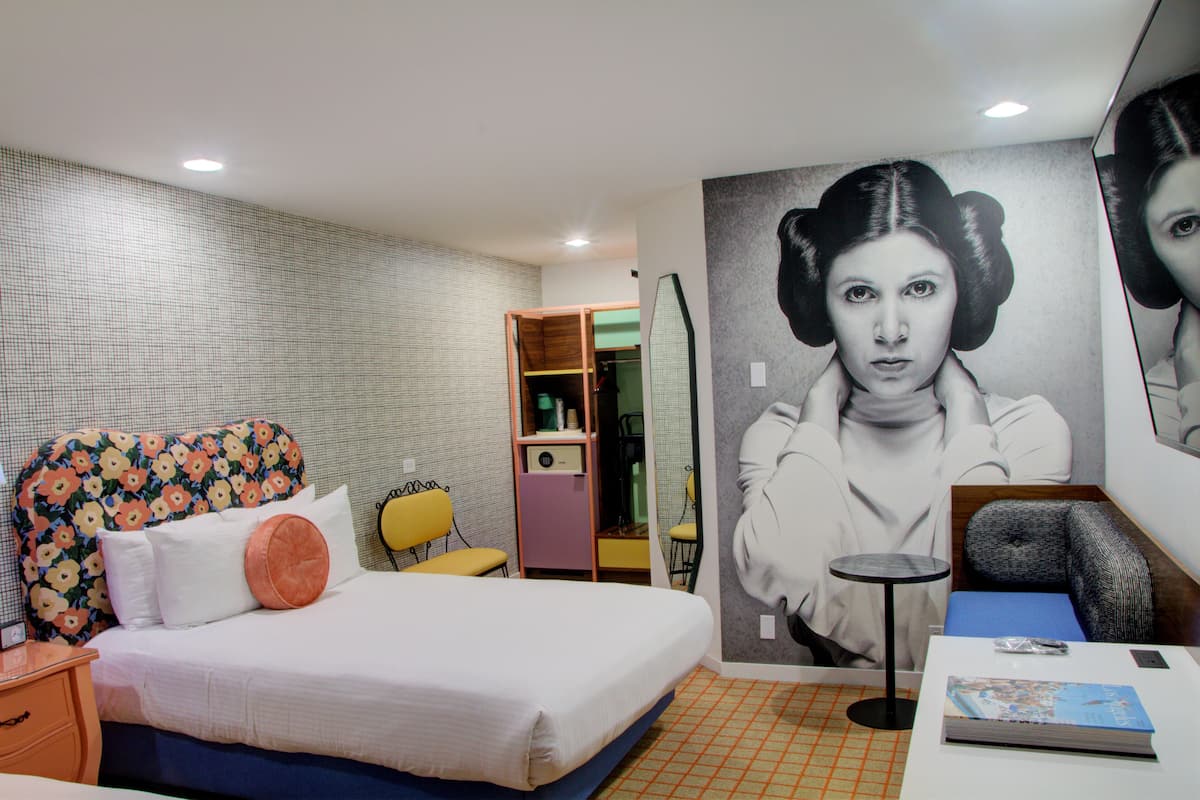 Een slaapkamer met een bed, een stoel, een tafeltje en een spiegel.