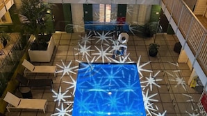 Ein Poolbereich im Innenbereich mit blauer Wasseroberfläche, umgeben von Liegestühlen und Topfpflanzen.