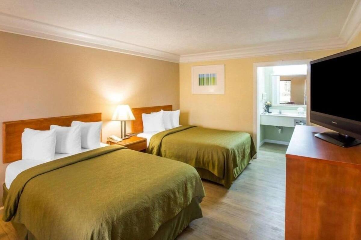 Habitación de hotel con dos camas, televisión, escritorio y baño a la vista, abierto.
