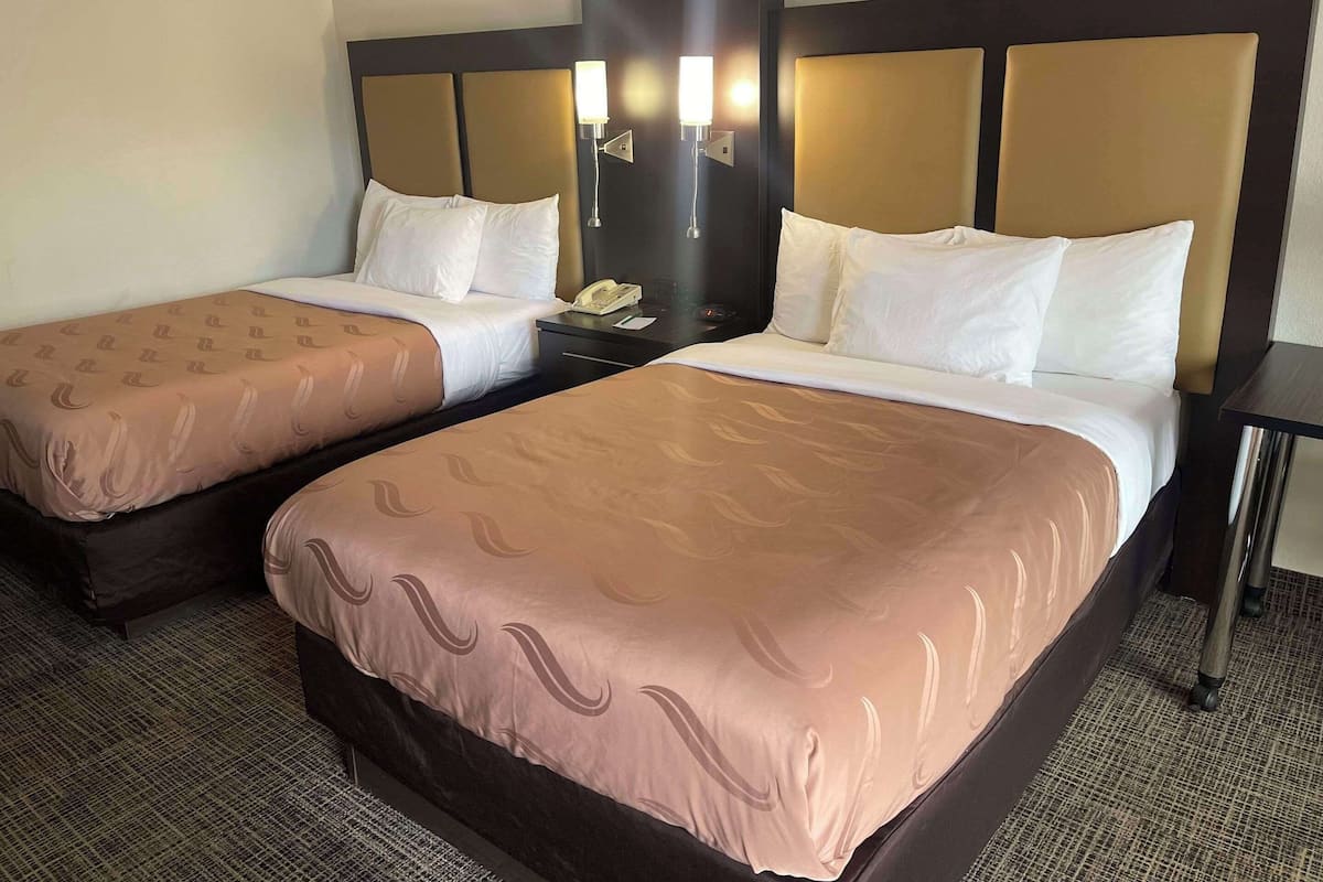 Habitación de hotel con dos camas, cada una con cabecera, mesita de noche y lámpara.