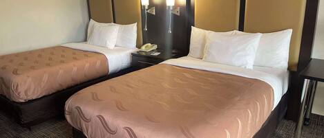A hotel room with two beds, each with a headboard, a nightstand, and a lamp.