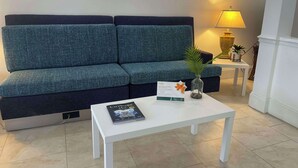 A modern living room with a blue sofa, a white coffee table with a book, a lamp, and a small plant. - Quality Inn Dalton Central (Dalton)
