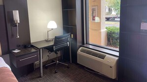 A hotel room with a desk, chair, lamp, air conditioning unit, and a window with a view of the outside. - Quality Inn Dalton Central (Dalton)