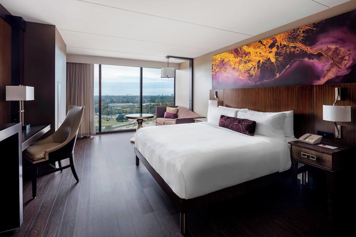 A modern hotel room with a large bed, a desk, a chair, and a view of the city.