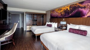 A hotel room with two beds, a desk, a chair, a TV, and a large abstract painting on the wall.