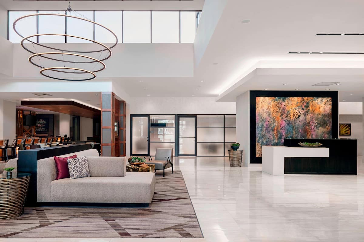 A spacious lobby with a modern reception desk, a large abstract painting, and a high ceiling with a circular light fixture.