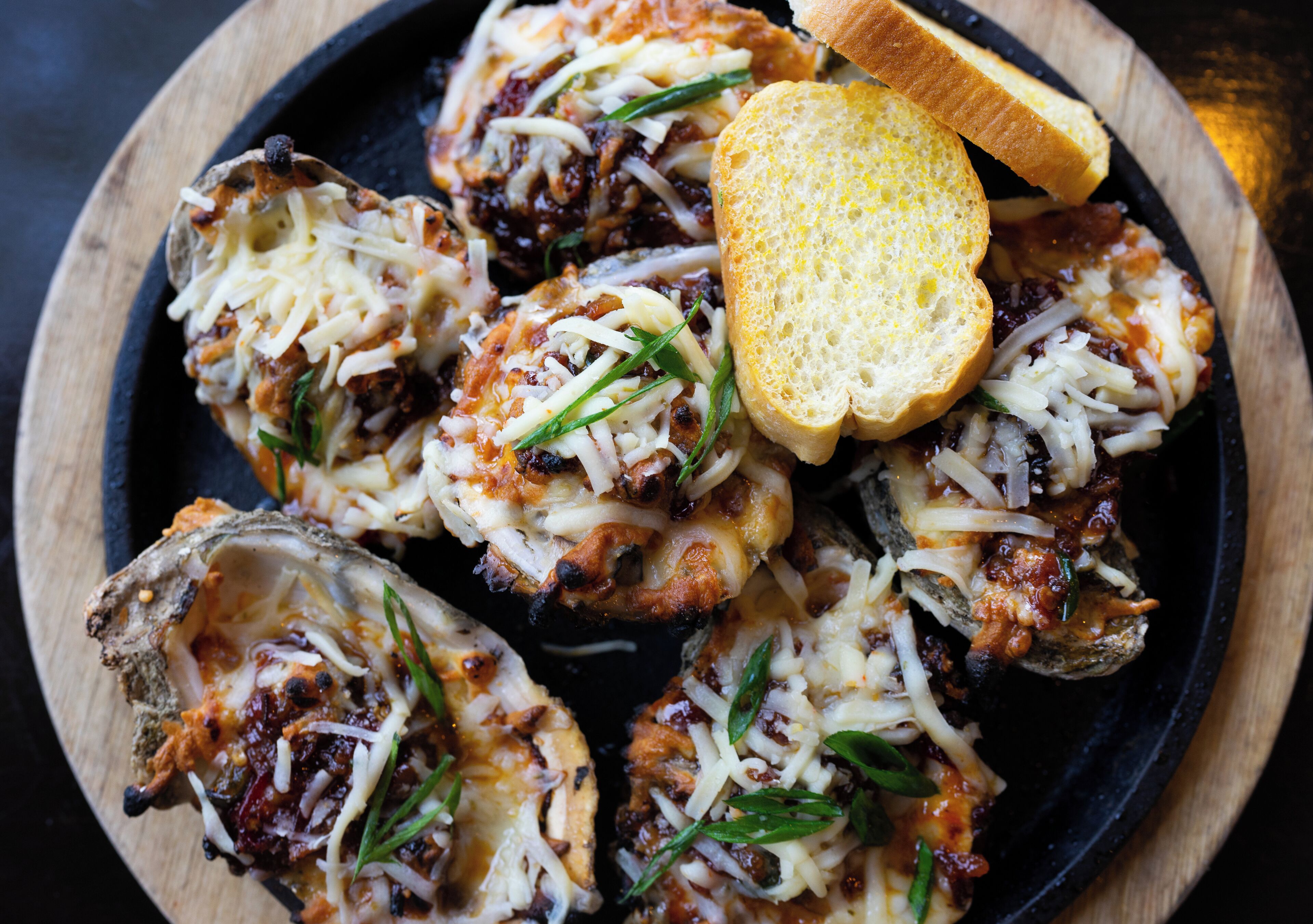 Een bord met gevulde champignons, belegd met kaas en kruiden, samen met sneetjes brood.
