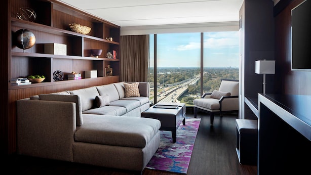 A modern living room with a large sofa, a coffee table, and a bookshelf. There is a large window with a view of a cityscape.