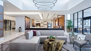 A modern lobby with a sectional sofa, a gold table, and a large window offering a view of the interior.