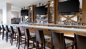 A bar area with a long counter, multiple bar stools, and a television mounted above.