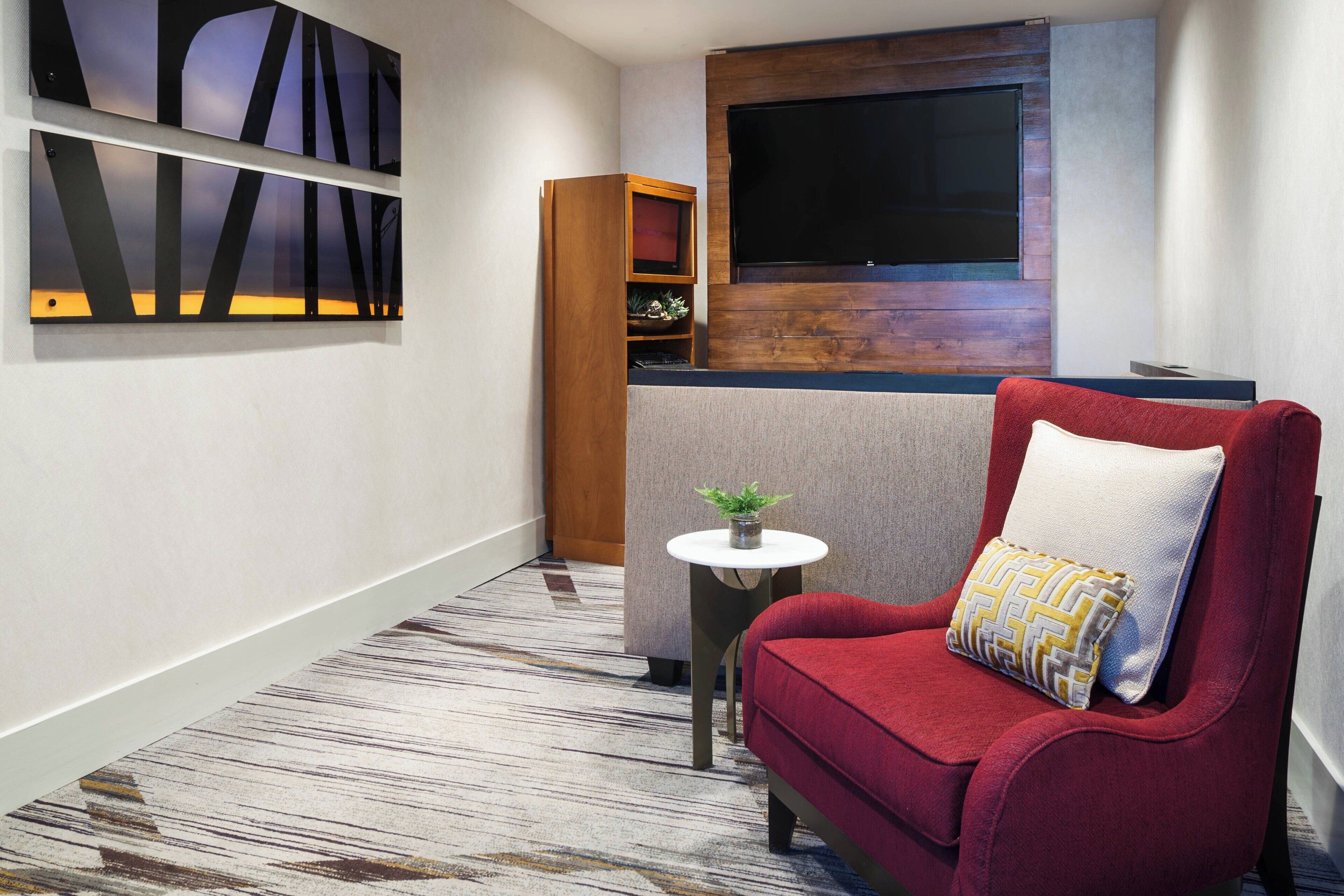 A modern hotel room with a red sofa, a small round table with a plant, and abstract wall art.